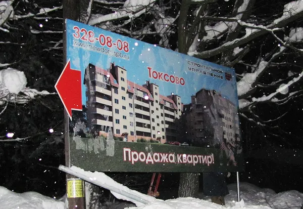 Уличный информационный щит 'Токсово - Продажа квартир' с указателем.