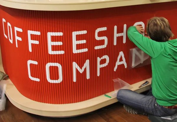 Процесс оклейки барной стойки кофейни виниловыми буквами.